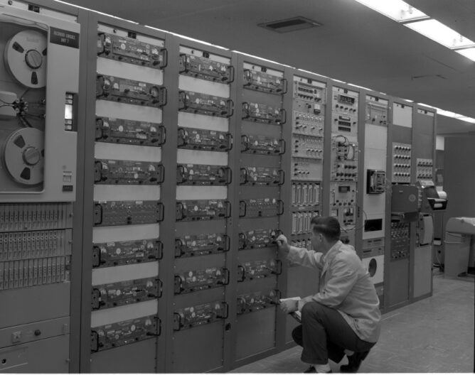 man with clip board inspecting a magnetic tape machine
